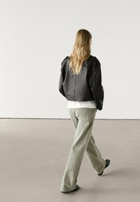 Svart läderkort jacka med axelaccenter, bärs över en vit topp, ihop med ljusgrå vida byxor och svarta skor.