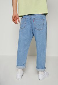 Vaaleansiniset farkut, joissa on käännetyt lahkeet, kahdella takataskulla, joissa on kaareva ommel, ja merkkilappu vyötäröllä. Valkoiset kengät ja sukat.