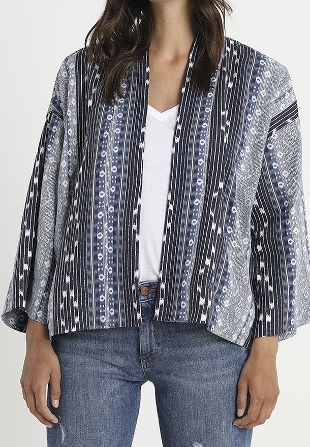 Veste de style kimono avec un motif géométrique bleu marine et blanc, dotée de larges manches et d'un design à l'avant ouvert. Fabriquée en tissu léger.
