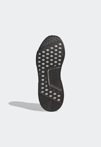 Svart Adidas sneaker sula med hexagonala uttag som avslöjar vitt material under, strukturerat greppmönster och logotypdetalj i mitten.