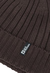 Bruine gebreide beanie met ribbelstructuur en een opgevouwen manchet. Voorzien van een zwart etiket met het "Jack Wolfskin" logo en een pootafdruk accent.