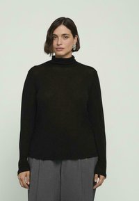 Czarna, długa bluzka z golfem wykonana z lekkiego materiału, charakteryzująca się luźnym krojem i miękką teksturą, zestawiona z szarymi spodniami w pliski.