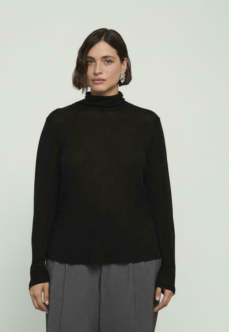 Czarna, długa bluzka z golfem wykonana z lekkiego materiału, charakteryzująca się luźnym krojem i miękką teksturą, zestawiona z szarymi spodniami w pliski.