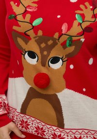 Röd jultröja med en ren som har en röd pom-pom-näsa och horn dekorerade med gröna och röda paljetter.