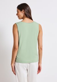 Haut sans manches vert avec un col arrondi et des détails de couture subtils à l'arrière. Tissu doux avec une coupe décontractée, assorti à un pantalon léger.