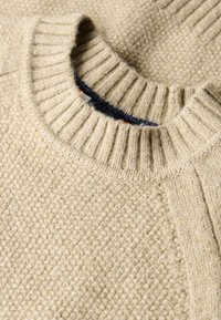 Suéter de punto beige con cuello redondo acanalado, que presenta un patrón texturizado y un forro interior suave en color marino.