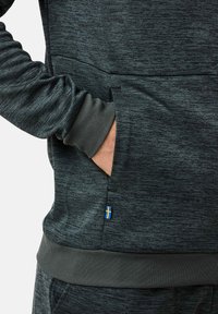 Dark gray hoodie made of textured fabric with a kangaroo pocket, ribbed cuffs, and a small Swedish flag accent at the hem.