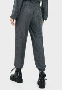 Czarne, błyszczące dresy z elastycznym pasem w talii oraz zwężanymi kostkami, połączone z masywnymi czarnymi butami z ćwiekami.