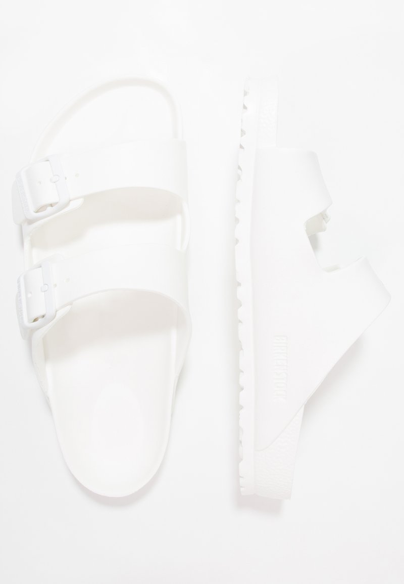 Sandali bianchi con due cinturini regolabili, suole piatte e lisce, e un motivo di battistrada testurizzato, caratterizzati da un design ritagliato su un lato.