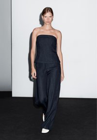Tmavě modrý bezramínkový top v kombinaci s volnými tmavě modrými kalhotami. Model má na sobě bílé boty s špičatou špičkou. Jednoduchý, čistý design.