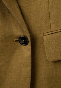 Približan posnetek rjave teksturirane jakne s črnim gumbom in žepom s preklopom na sprednji strani.