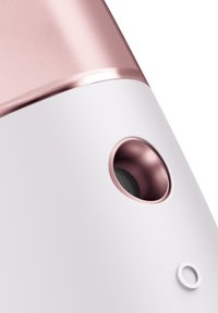 Dispositif sans fil avec une finition blanche mate et des accents en or rose. Bouton circulaire en bas, ouverture ronde proéminente révélant une texture en maille.