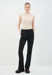 Top sin mangas beige con tres botones decorativos, combinado con pantalones negros ajustados y zapatos de plataforma de burdeos oscuro. Diseño sencillo, textura suave.