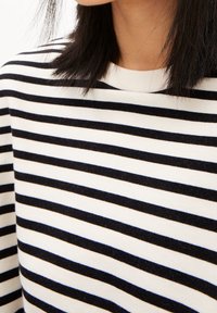 Gestreifter Pullover in Schwarz-Weiß mit rundem Ausschnitt und weichem, strukturiertem Stoff. Die Streifen haben die gleiche Breite und sind gleichmäßig verteilt.