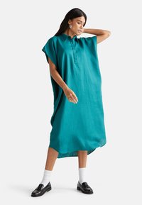 Turkusowa lniana sukienka koszulowa z kołnierzykiem, krótkimi rękawami i bocznymi rozcięciami; zestawiona z czarnymi mokasynami i białymi skarpetkami.
