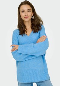 Jasnoniebieski, oversize sweter z dekoltem w serek, prążkowanymi mankietami i dołem. Miękka faktura, długie rękawy i luźny krój.
