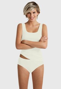 White tankini set featuring a square neckline and side cut-out detail. Soft fabric with a smooth texture. Model poses with crossed arms.