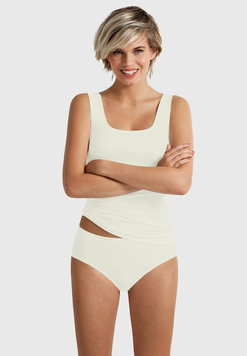 White tankini set featuring a square neckline and side cut-out detail. Soft fabric with a smooth texture. Model poses with crossed arms.
