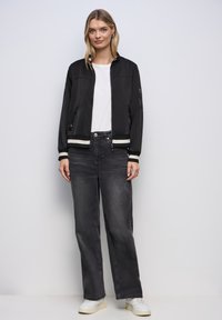 Czarna bomberka z paskowanymi mankietami, noszona na białej koszuli. Połączona z wysokimi, luźnymi ciemnoszarymi dżinsami oraz białymi trampkami.