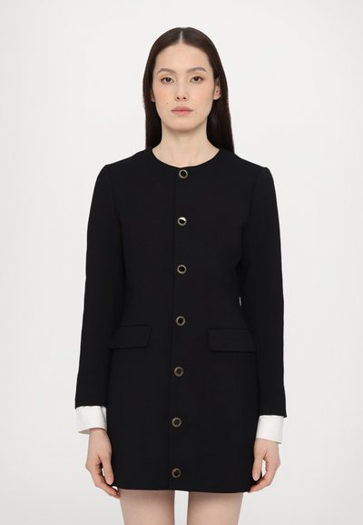 Manteau noir avec des détails de boutons dorés, design ajusté, deux poches avant, manches longues et poignets blancs contrastants. Texture lisse.
