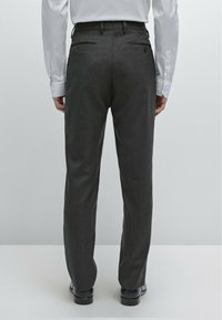 Grau maßgeschneiderte Hosen mit einem strukturierten Stoff, zwei Gesäßtaschen und einem Slim-Fit-Design, kombiniert mit schwarzen Schuhen und sichtbaren Hemdmanschetten.