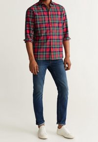 Rød og grønternet langærmet skjorte, parret med blå slim-fit jeans og hvide sneakers, har rullede ærmer og krave med knapper.