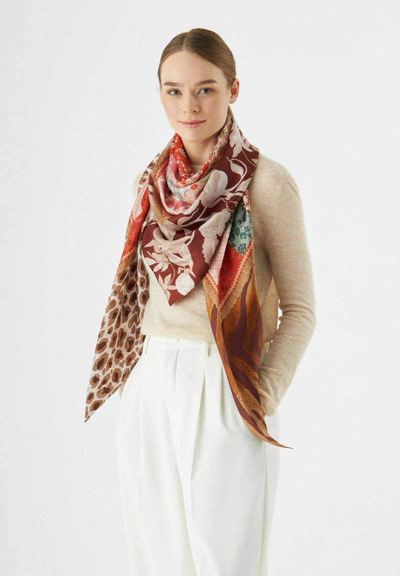 Foulard en soie avec des motifs variés : floral en rouge et vert, imprimé léopard en brun, et formes abstraites en rouille. Forme triangulaire, couleurs vives.