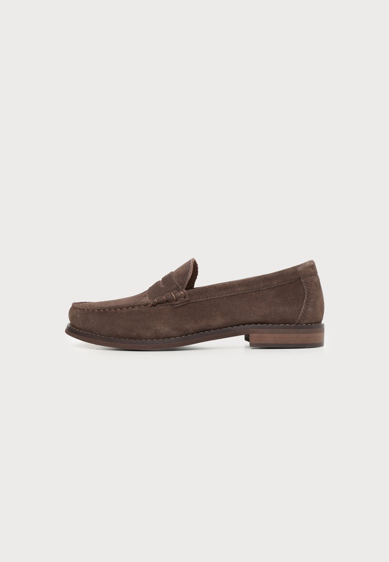Mocassin homme en cuir suédé marron avec petit talon empilé et couture moc toe sur fond blanc.