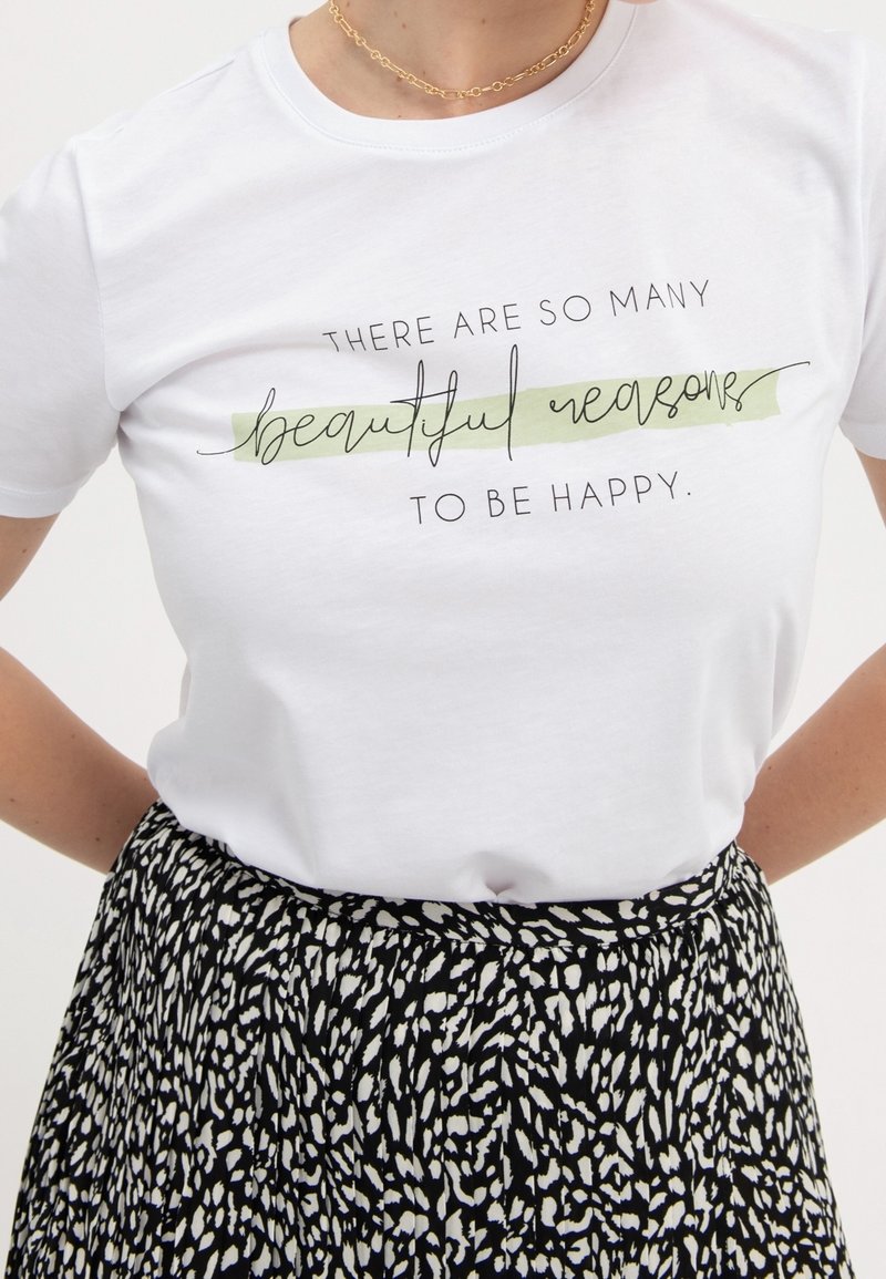 T-shirt blanc avec texte noir ""There are so many beautiful reasons to be happy,"" associé à une jupe à motifs noir et blanc.