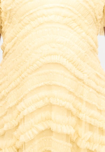 Κίτρινο ύφασμα με οριζόντιες στρωματοποιημένες βολάν που δημιουργούν μια υφασμένη, κυματιστή υφή σε ρούχο.