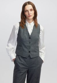 Gleichfarbiger Wollweste mit Karomuster, mit V-Ausschnitt, fünf Knöpfen und zwei Fronttaschen, kombiniert mit einem weißen Button-Up-Hemd.