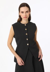 Zwarte mouwloze top met een ronde halslijn en vijf gouden knoopsluitingen. Heeft een strakker, minimalistisch ontwerp en een soepele stoftextuur.