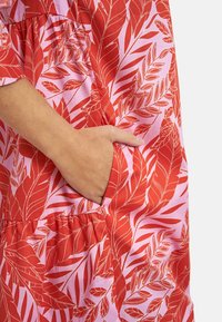 Red and pink dress with a leafy print; features a side pocket, gathered waist, and smooth cotton texture.