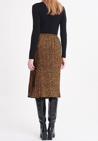 Brun plisserad midikjol med svart leopardmönster, kombinerad med en figurnära svart långärmad topp och knähöga svarta stövlar.