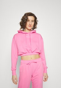 Felpa corta rosa con cappuccio, caratterizzata da un logo frontale e orlo a costine. Si abbina a pantaloni della tuta rosa coordinati, realizzati in un tessuto morbido.