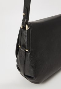 Borsa a tracolla in pelle nera con superficie texturizzata, fondo arrotondato e dettagli in metallo dorato sulla tracolla.