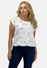 Biała bluzka z krótkimi rękawami, zdobiona czarnym wzorem ptaków, zebranym dołem i lekkim materiałem, w połączeniu z ciemnogranatowymi spodniami.