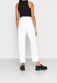 Bílé upravené kalhoty s ohrnutými cuffy, stylizované s černým upnutým tílkem a masivními černými slip-on botami, ukazující čistý, minimalistický vzhled.