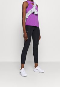 Lila sporttopp med utskärning, svarta tajta leggings och vita sneakers. Grå sweatshirt knuten runt midjan. Släta texturer genom hela outfiten.