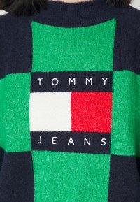 Strickpullover mit Blockdesign in Grün, Marineblau und Rot. Enthält das "TOMMY JEANS"-Logo in Weiß auf einem dunklen Streifen. Weiche Ästhetik.