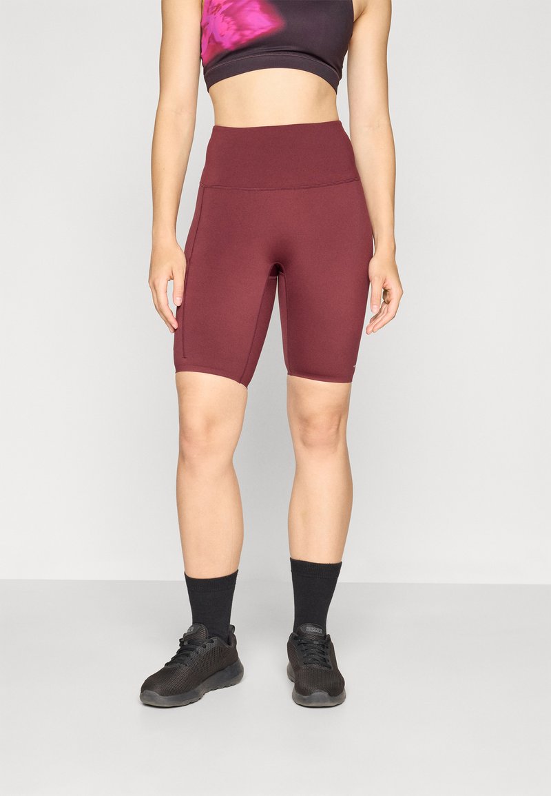 Bordo bicikle kratke hlače s visokim strukom, izrađene od rastezljivog materijala. Uparene s crnim crop topom s ružičastim tie-dye detaljima i crnim sportskim cipelama.