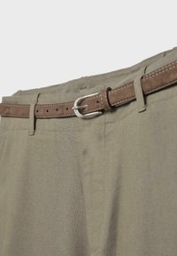 Pantalon kaki avec une fine ceinture en daim marron passée dans les passants, avec une boucle argentée fixée sur le côté droit.