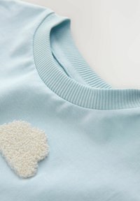 Tricou din bumbac albastru deschis, cu un design texturat de norișor alb pe față. Gulerul este cu bordură, adăugând detaliu și contrast.