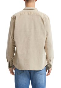 Beige corduroy overhemd. Lange mouwen met knoopmanchetten, achterste yoke naaddetail, gebogen zoom, zachte textuur en een iets ruime pasvorm.