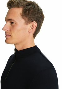 Maglione lavorato a maglia nero con colletto alto e dettaglio con zip. Il tessuto appare liscio e la vestibilità è aderente al corpo.