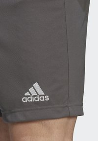 Pantalones cortos deportivos grises hechos de una tela suave, con un logo de Adidas bordado en blanco en el lado izquierdo, y un diseño simple sin patrones.