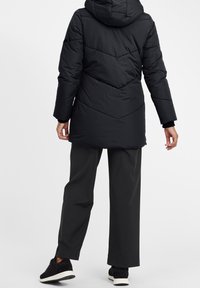 Svart puffjacka med huva, med ett chevron-kviltat mönster. I kombination med löst sittande svarta byxor och svarta sneakers.