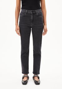 Zwarte high-waisted jeans met een rechte pijp, voorzien van voorzakken en een tonale stikselafwerking, gecombineerd met zwarte flats met decoratieve banden.
