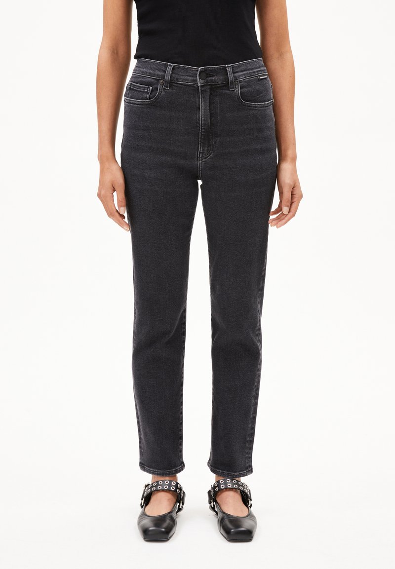 Zwarte high-waisted jeans met een rechte pijp, voorzien van voorzakken en een tonale stikselafwerking, gecombineerd met zwarte flats met decoratieve banden.