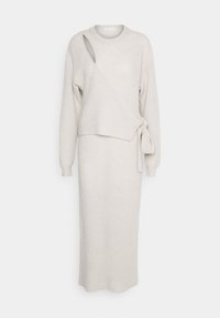 Robe tricotée côtelée gris clair avec un décolleté asymétrique et un lien à la taille. Manches longues et longueur cheville. Texture douce.